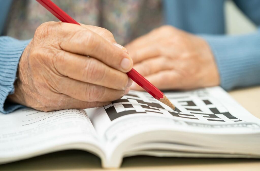 A senior holding a red pencil while working on a crossword puzzle