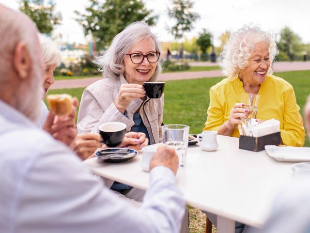 Group of seniors sitting at a park outdoor cafe, enjoying coffee together and smiling at the table.